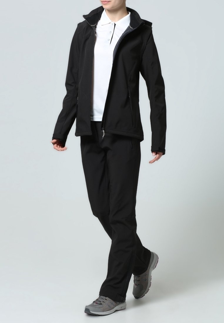 Chaqueta de softshell negra con un diseño ajustado, cremallera frontal y capucha, combinada con pantalones negros a juego y zapatos de senderismo grises.