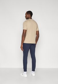 Camiseta beige de manga corta combinada con pantalones joggers azul marino y zapatillas blancas. Tela suave; ajuste relajado; detalle sutil del logo en la manga.