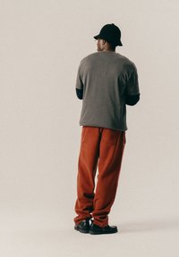 Hallide hall sleeves shirt, punased laiad püksid ja mustad jalanõud. Riietus on lõdva lõikega ja minimaalsete aksessuaaridega.