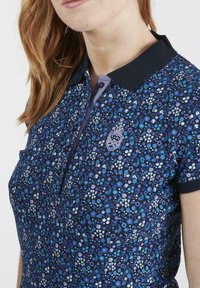 Polo shirt navy avec un motif floral en bleu et blanc. Doté d'un col, d'une patte de boutonnage à trois boutons et d'un logo brodé.