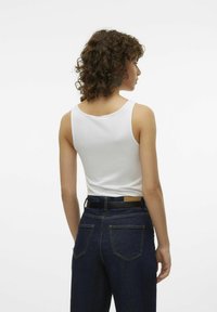 Witte katoenen tanktop gecombineerd met donkerblauwe denim high-waisted broek. De outfit heeft een zwarte riem en een eenvoudige achterkant zonder versieringen.
