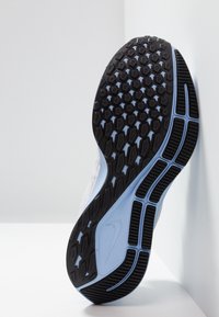 Suola in gomma nera con motivo a esagoni, intersuola di un blu chiaro e materiale superiore bianco texturizzato. Logo Nike visibile sul lato.