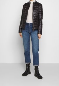 Svart puffjacka med kviltad design, hög krage och dragkedjestängning, tillsammans med ljusblå raka jeans och svarta snörkängor.