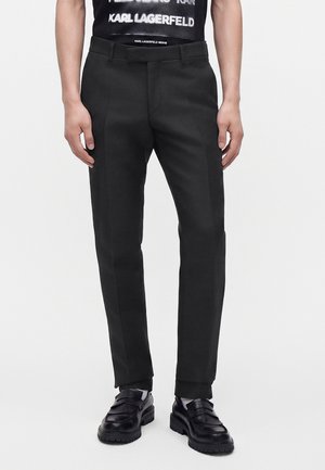 Mand iført slanke sorte bukser, sorte læder loafers og en sort t-shirt med hvid tekst.