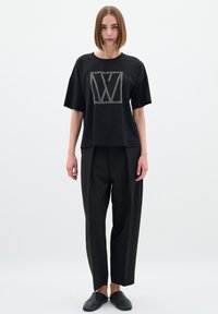 T-shirt noir à manches courtes avec un grand logo clouté argenté dans un carré. Associé à un pantalon noir ample et des chaussures noires à enfiler.