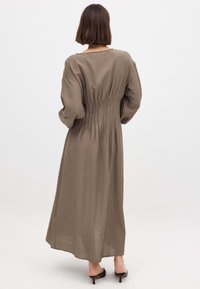 Abito lungo e aderente in un colore oliva tenue. Realizzato in un tessuto leggero con dettagli arricciati sul retro e maniche ampie e voluminose.
