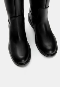 Bottines noires en cuir avec des orteils arrondis et une texture lisse. Présente une couture minimale et une semelle en caoutchouc plate. Pas de matériel visible.