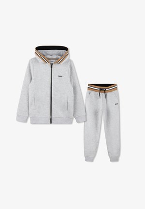 Felpa grigia con zip e colletto a strisce nere e dorate, abbinata a pantaloni jogger coordinati con vita a cordoncino.