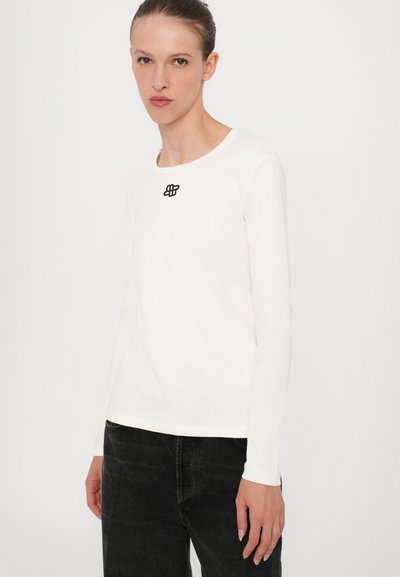 Long-sleeve shirt in white ribbed fabric with a round neckline and a small black embroidered logo on the chest.