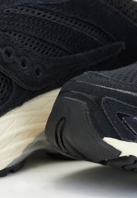 Zapatillas deportivas negras que combinan una mezcla de materiales transpirables de malla y ante, con una suela de goma texturada y sutiles acentos en blanco.