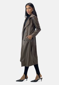 Brun imitationsläder trenchcoat med dubbelknäppt design, breda slag och sidofickor. Matchas med svarta högklackade mules.