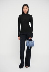 Pulover negru cu model striat, design ajustat, asortat cu blugi largi în nuanțe întunecate. Poartă o geantă mică, structurată, de culoare bleu deschis, cu accesorii din argint.