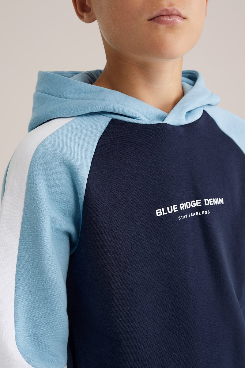 Námornícky mikina s svetlomodrými rukávmi a akcentami. Obsahuje klokanie vrecko a potlačený logo "BLUE RIDGE DENIM STAY FEARLESS." Mäkká tkanina.