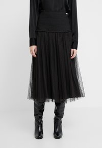 Falda midi de tul negra con cintura fruncida y un sutil patrón de lunares, combinada con botas de cuero negras hasta la rodilla.