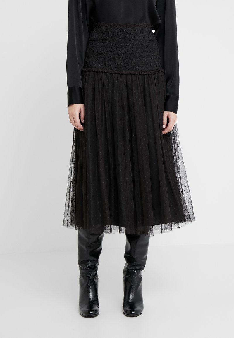 Falda midi de tul negra con cintura fruncida y un sutil patrón de lunares, combinada con botas de cuero negras hasta la rodilla.