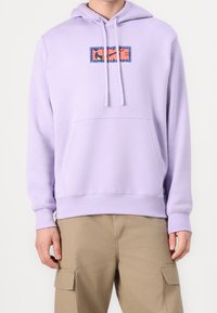 Lavendelfärgad huvtröja med en framficka, prydd med en flerfärgad grafisk patch inramad i blått. Mjuk tyg, avslappnad passform.