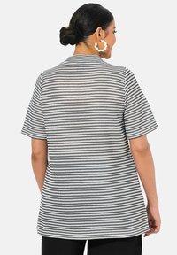 Černobílý pruhovaný top s krátkým rukávem, volným střihem, texturovanou tkaninou a rovnými okraji, z pohledu zezadu.