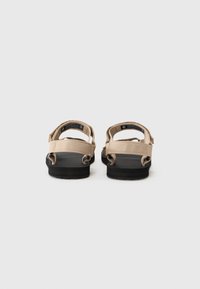 Beige sandaler med sorte gummisåler, med justerbare remmer og en teksturert fotbed for grep. Minimalistisk design med forsterket søm.