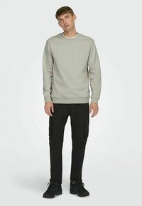 Grå genser med rund hals, kombinert med svarte cargobukser med sidelommer. Antrekket fullføres med svarte treningssko.