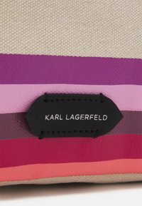 Canvas-handväska med lila, rosa och korallränder. Har en svart läderetikett med vit text "KARL LAGERFELD". Texturerad tyg.