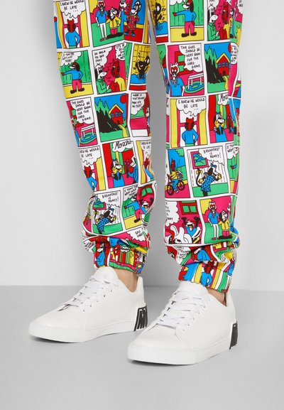 Calças de jogging coloridas com padrões de bandas desenhadas e vários personagens de cartoon. Ténis brancos com detalhes em preto e solas texturizadas.