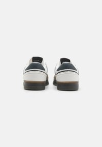 Hvide sneakers med marineblå detaljer, glat læderoverdel og gummisål. Har minimal branding på hælen og kontrasterende syninger.