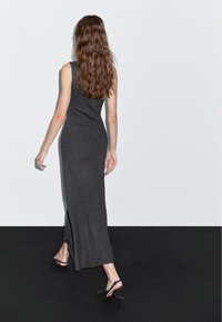 Robe maxi sans manches gris charbon avec une silhouette ajustée, dotée d'une fente latérale et d'une texture douce, associée à des talons slingback noirs.