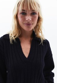 Maglione a coste blu navy con scollatura a V e colletto. Presenta una texture morbida e maniche lunghe, offrendo un aspetto aderente ma confortevole.