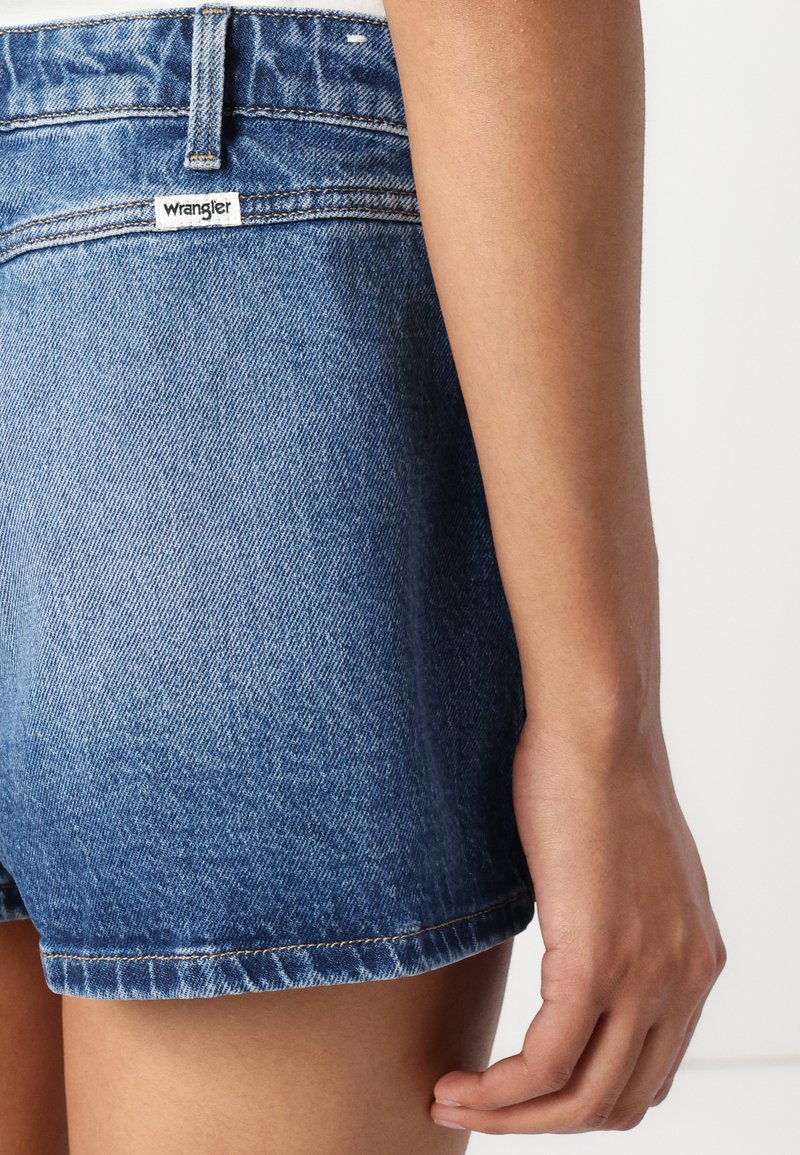 Jasnoniebieskie szorty dżinsowe o kluczowym kroju, z miedziowym przeszyciem i metką Wrangler na tylnej kieszeni. Gładka faktura.