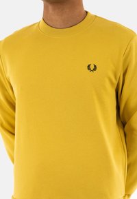 Sudadera amarilla de mezcla de algodón, con cuello redondo, puños acanalados y un pequeño logo negro bordado en el pecho.