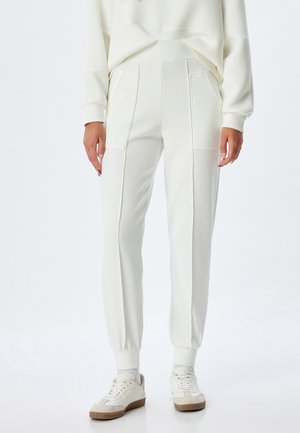 Witte sweatpants met geribbelde boorden en zijzakken, met een gladde textuur en een iets relaxte pasvorm, gecombineerd met witte sneakers.