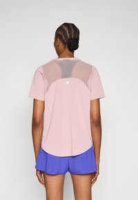 Ροζ αθλητική μπλούζα με κοντά μανίκια, διαθέτει πλέγμα στην πίσω πλευρά, στρογγυλεμένο τελείωμα και μικρή λεπτομέρεια με λογότυπο στο κέντρο του άνω μέρους της πλάτης.