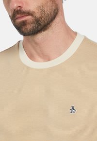 Lichtbeige gestreepte T-shirt met ronde hals en ribgebreide halslijn. Heeft een klein blauw pinguïnlogo op de linkerkant van de borst. Zachte textuur.