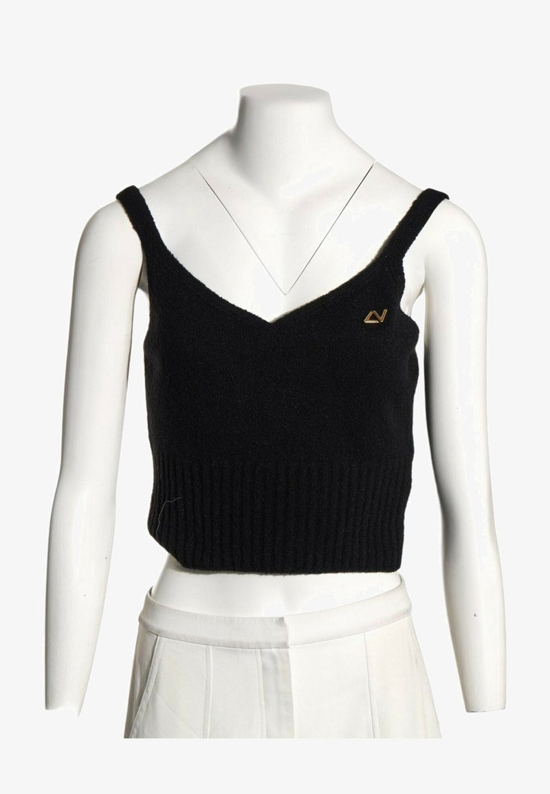 Débardeur court en maille noire avec fines bretelles sur un torse de mannequin blanc, associé à un pantalon blanc taille haute.