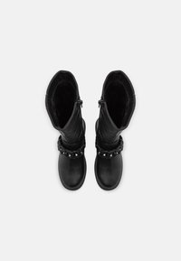 Bottes en cuir noir avec une tige haute, dotées d'un accent chaîne autour de la cheville, d'une doublure texturée et d'un design à bout lisse et arrondi.