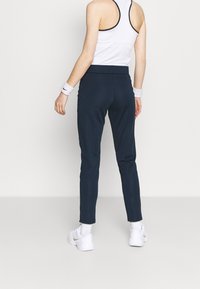 Marinblåa träningsbyxor med avsmalnande passform, utrustade med elastisk midja och slät tygstruktur. Matchas med vita träningsskor och handledsband.