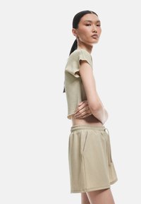 Set coordinato beige composto da una maglietta cropped in tessuto testurizzato con maniche corte, abbinata a pantaloni corti con vita elastica.