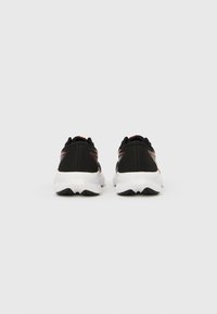 Svarte treningssko med hvite såler, med røde detaljer og en teksturert overdel for pusteevne. Designet med en polstret hæl for komfort.