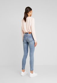 Suéter rosa claro combinado con jeans ajustados de un azul medio. Los jeans presentan un acabado desgastado y un parche de cuero marrón en la parte trasera. Zapatillas blancas.