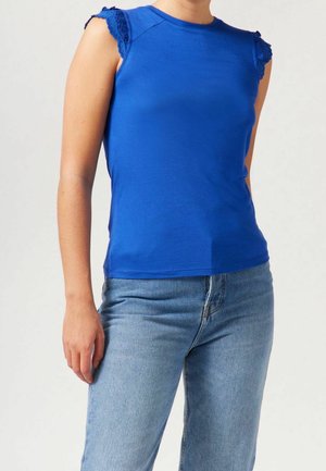 Haut bleu sans manches avec bordure en dentelle festonnée aux épaules, fabriqué en tissu léger ; associé à un jean en denim clair.