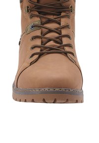 Bota de cuero marrón con punta redonda, ojales de metal y cordones marrones. Presenta una suela de goma con un patrón de relieve texturizado.
