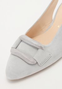 Chaussure plate en suède gris avec un bout pointu, ornée d'un accent en nœud en argent texturé sur le devant et d'une doublure intérieure lisse.