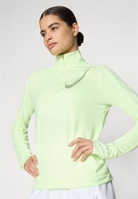 Light green, long-sleeve quarter-zip top in smooth fabric, featuring a subtle Nike logo on the chest. Slim fit with textured accents.
