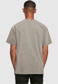 Camiseta de algodón gris con un corte relajado, mangas cortas y cuello redondo. Presenta una textura lavada y costuras visibles a lo largo de los bordes.
