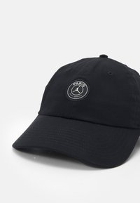 Black baseball cap made of cotton with a curved brim, featuring a round patch with "PARIS" and a logo on the front.