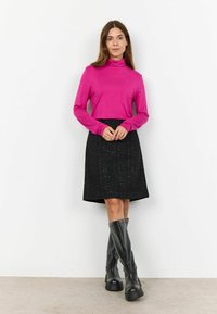 Haut fuchsia à manches longues avec un col haut, associé à une jupe en A noire texturée et des bottes à plateforme noires jusqu'aux genoux.