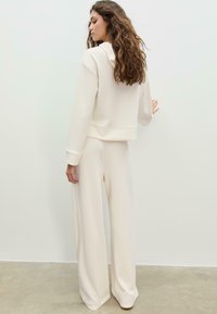 Beige kort hoodie med dragsko på huvan och långa ärmar, kombinerad med vida beige byxor. Slät tyg med minimal textur.