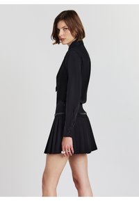 Une chemise noire à manches longues associée à une jupe plissée noire. La tenue présente un design structuré et une silhouette cintrée.