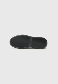 Semelle de chaussure en caoutchouc noir avec une texture striée, des bords arrondis et un léger talon. Présente un branding subtil le long du centre.