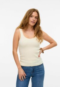 Ljusbeige ribbad tanktop med rundad halsringning och breda axelband, ihop med blå denimjeans. Slät textur, åtsittande silhuett.